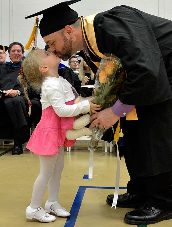 Graduating father giving his young child a kiss after receiving his diploma